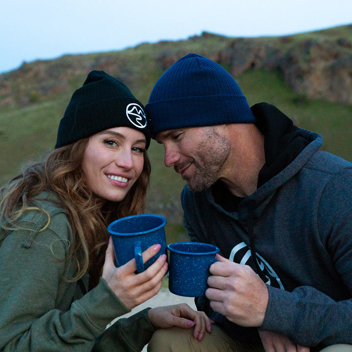 Smiling woman in green hoodie and black Mtn Flo beanie with smiling man wearing dark gray hoodie sweater with black interior and white Mtn Flo logo on chest